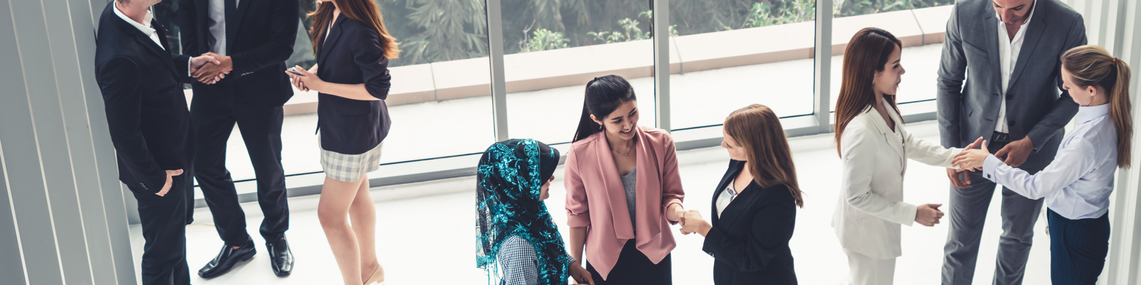 Overhead view of diverse business professionals networking and shaking hands in groups in a modern office lobby with floor-to-ceiling windows