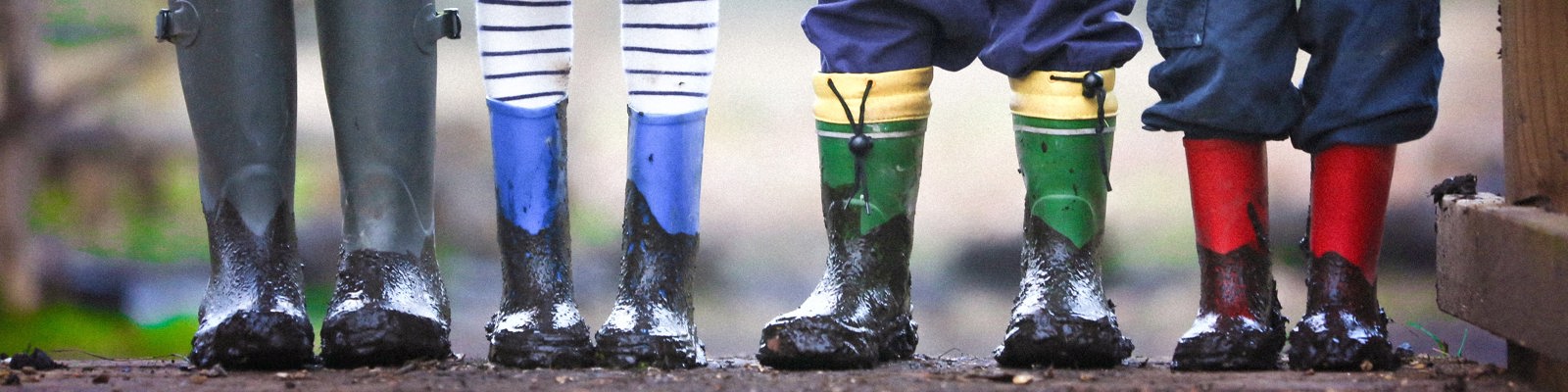 Photo of 3 children and adult legs, showing their wellington boots muddy on a trail.